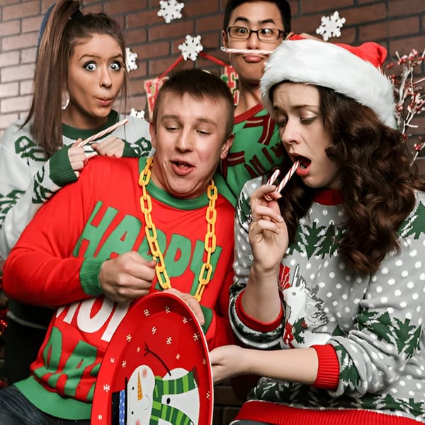 Four young adults in festive Christmas sweaters making funny faces and eating candy canes.