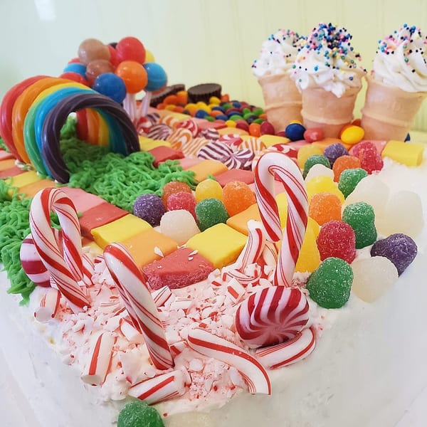 A vibrant candy land cake with a rainbow, ice cream cones, and various colorful candies.