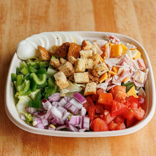 A vibrant salad with lettuce, green peppers, red onions, tomatoes, croutons, cheese, and ham.