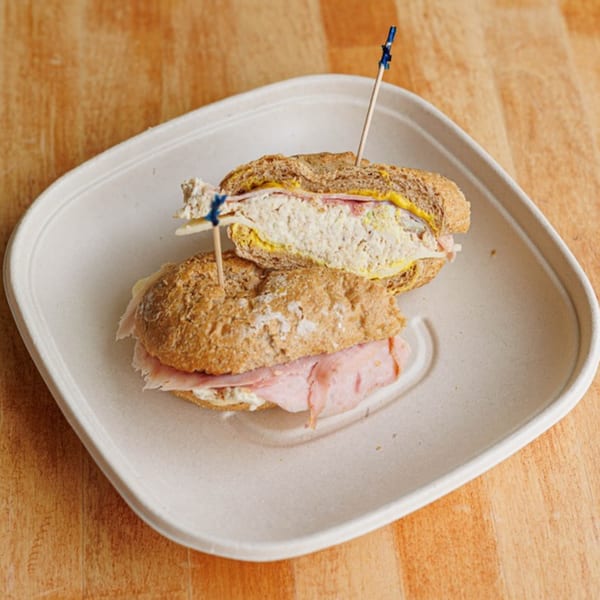 Two halves of a deli sandwich with ham, cheese, and mustard on a white plate.