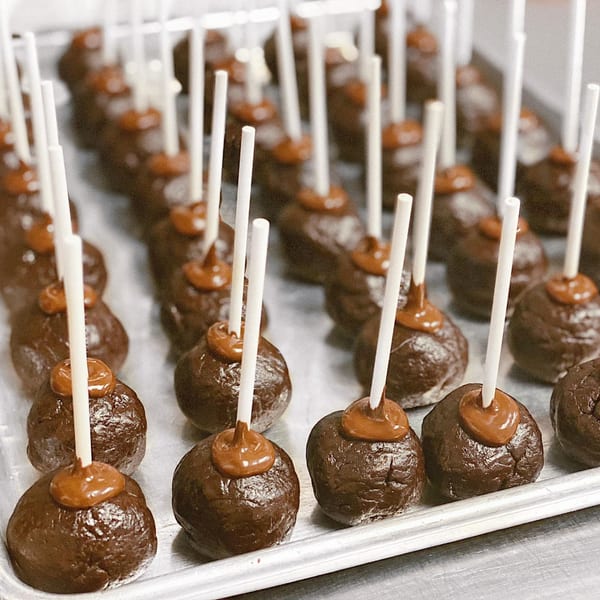 Rows of chocolate cake pops with caramel drizzle on a silver tray at eats & sweets bakery.