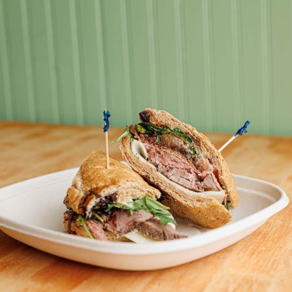 Two halves of a hearty sandwich with sliced meat, cheese, and greens on a white plate.