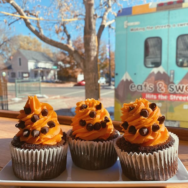 Three chocolate cupcakes with orange frosting and chocolate chips sit on a white plate by a window.