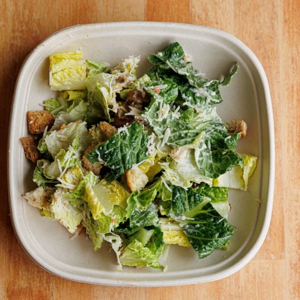 Caesar salad with romaine lettuce, croutons, and parmesan cheese in a light bowl on a wooden table.