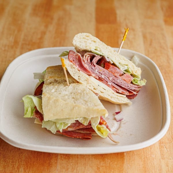 Two halves of a deli sandwich with salami, cheese, and lettuce on a white plate.